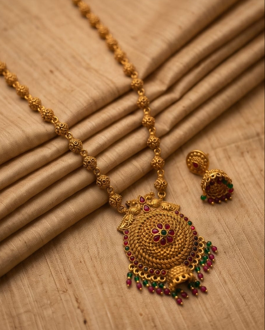 Gold necklace with intricate design and red and green gemstones on a beige fabric background