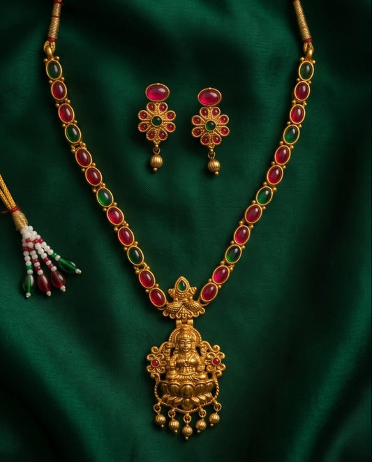 Gold necklace with red and green gemstones and matching earrings on a green fabric background