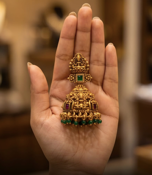 Gold and green gemstone jewelry piece held in a hand with a blurred background