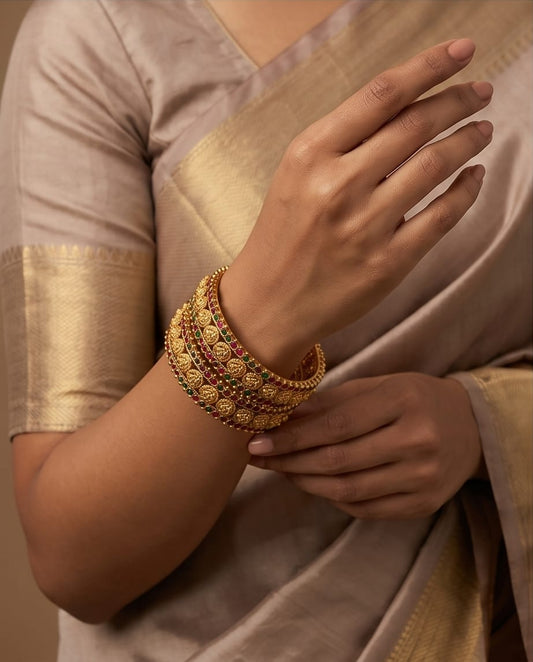 Close-up of a hand wearing gold jewelry with a beige saree background