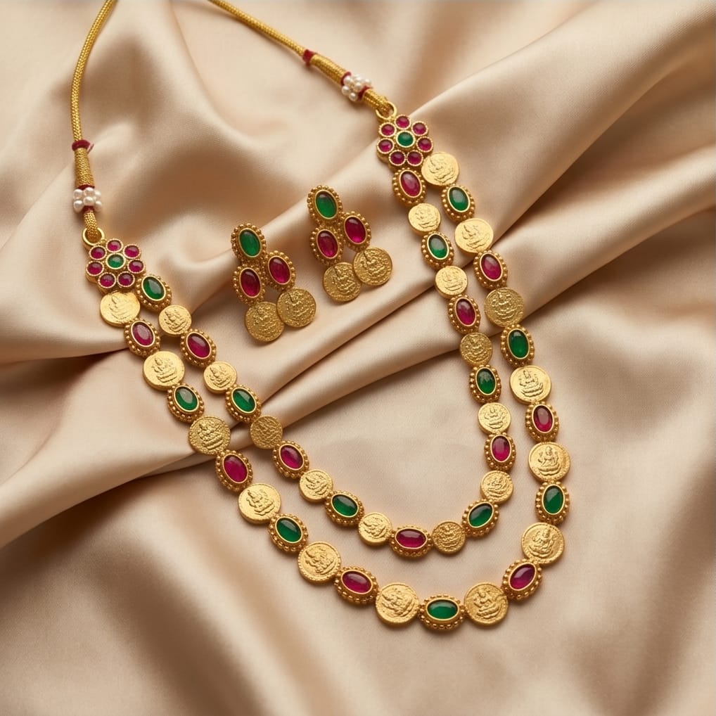 Gold necklace and earrings with red and green stones on a beige fabric background