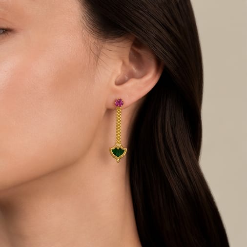 Gold earring with green gemstone worn by a person against a neutral background