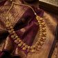 Gold necklace with red stones on a maroon saree with gold patterns