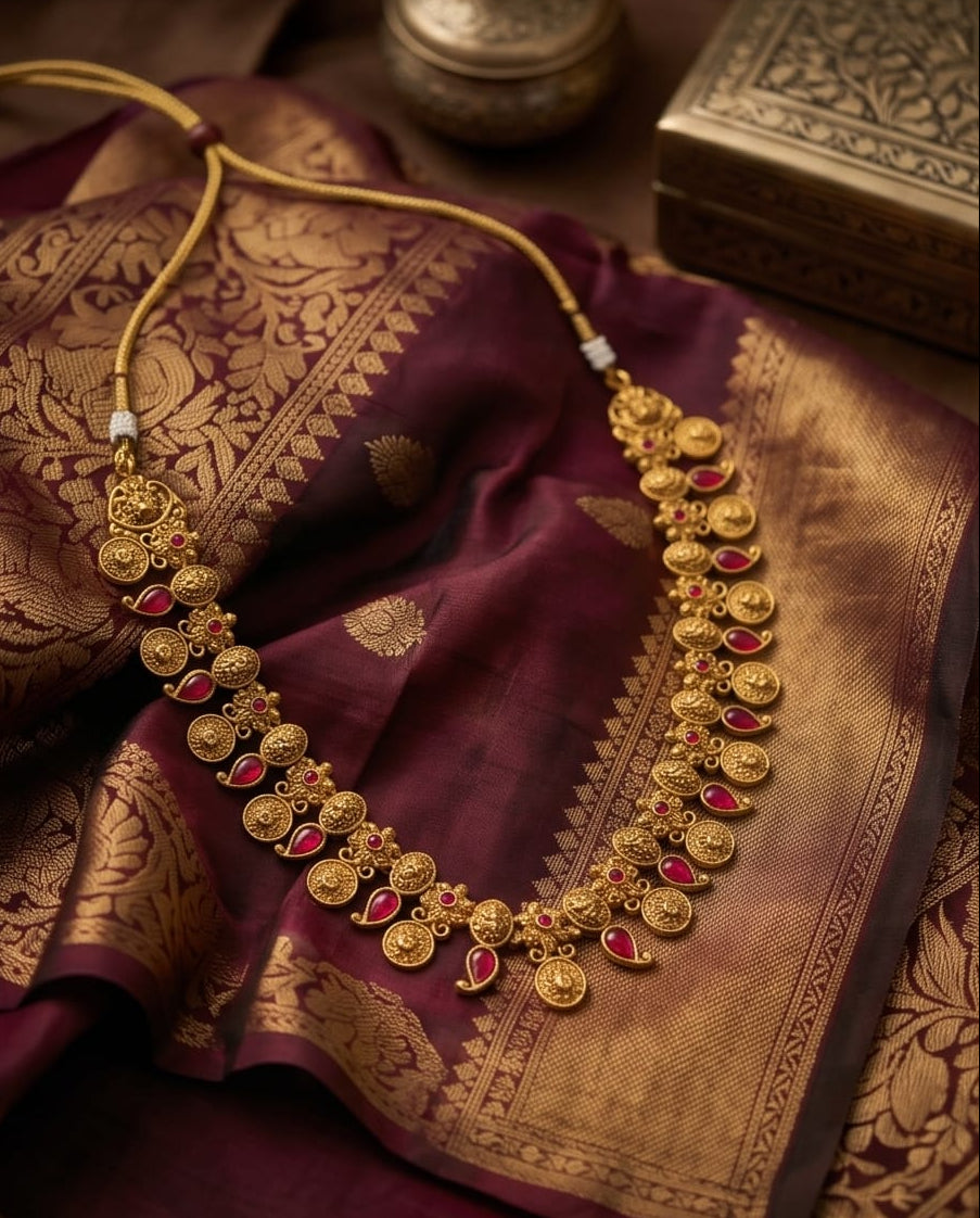 Gold necklace with red stones on a maroon saree with gold patterns