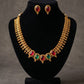 Gold necklace with red and green gemstones and matching earrings on a black stand against a gray background