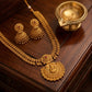 Gold necklace and earrings set on a wooden surface with a small brass lamp.
