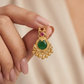 Gold earring with green gemstone held by a hand against a beige background