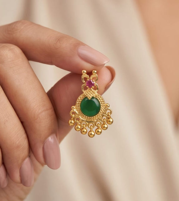 Gold earring with green gemstone held by a hand against a beige background