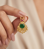 Gold earring with green gemstone held by a hand against a beige background