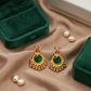 Gold earrings with green stones and pink gemstones on a beige fabric background.