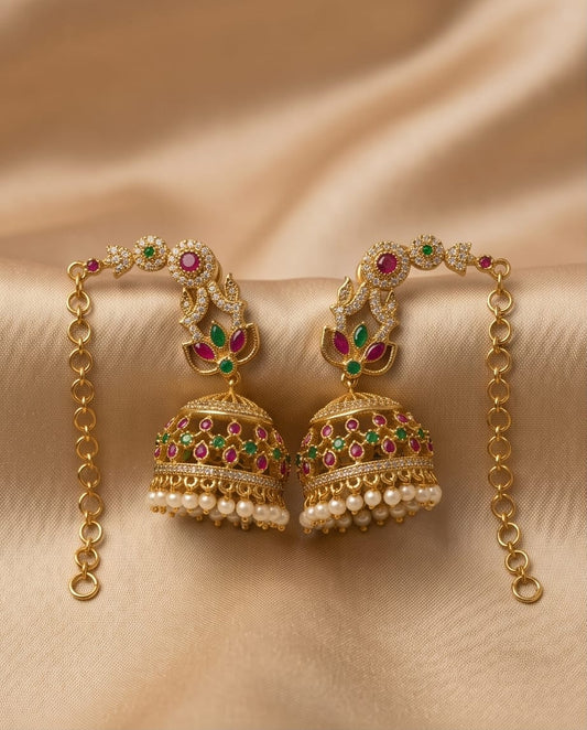 Ornate gold earrings with pearls and gemstones on a beige fabric background