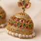 Gold jhumka with pearls, red and green gemstones on a beige background