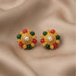 Pair of gold earrings with red and green gemstones on a beige fabric background
