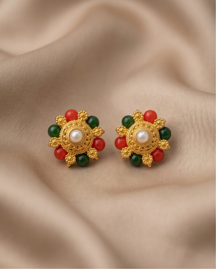 Pair of gold earrings with red and green gemstones on a beige fabric background