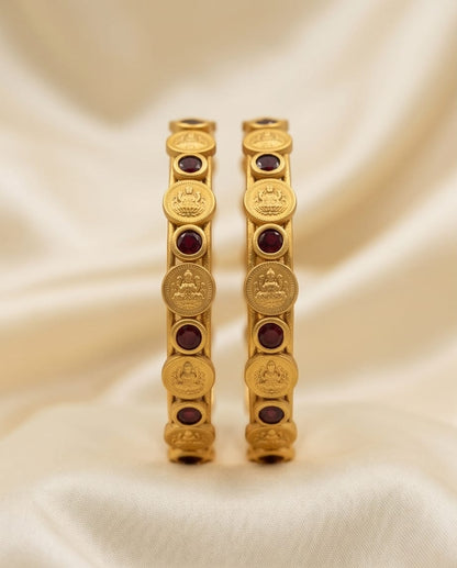 Pair of gold bangles with red stones on a beige fabric background