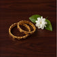 Two gold bangles with a white flower on a wooden surface