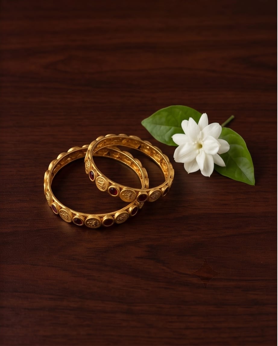Two gold bangles with a white flower on a wooden surface