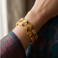 Gold bracelet with embedded stones on a wrist, wearing a patterned garment.