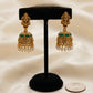 Gold earrings with green stones on a black stand against a beige background