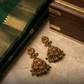 Gold earrings with green and red stones on a marble surface next to a saree and wooden box.