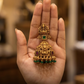 Gold and green gemstone jewelry piece held in a hand with a blurred background