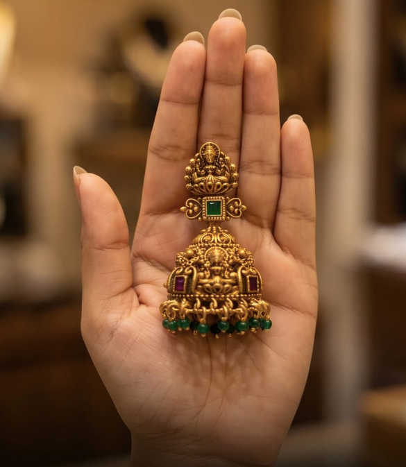 Gold and green gemstone jewelry piece held in a hand with a blurred background
