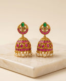 Pair of gold earrings with pink and green gemstones on a beige surface