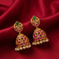 Ornate gold earrings with green and red stones on a red fabric background