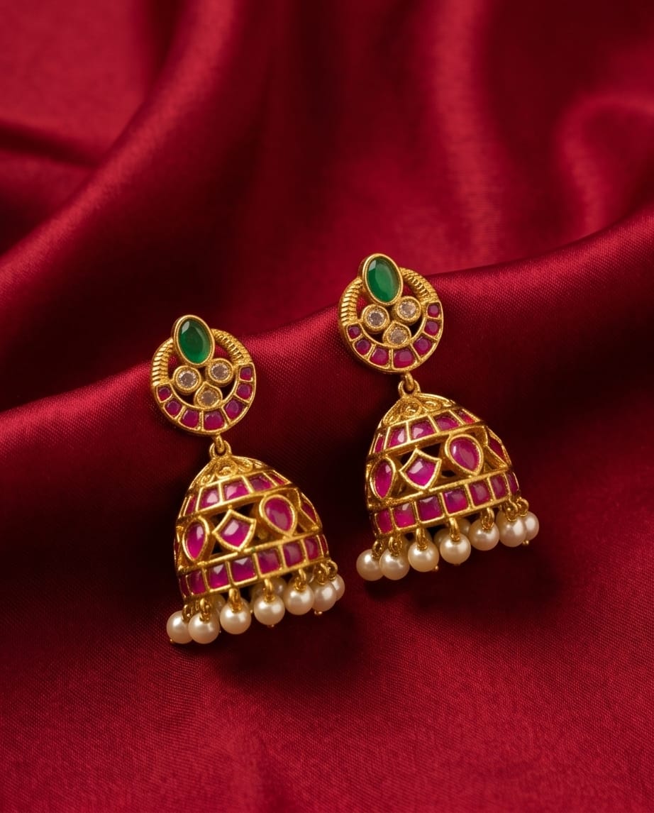 Ornate gold earrings with green and red stones on a red fabric background