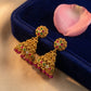 Gold earrings with colorful gemstones on a blue velvet stand with a pink flower petal.