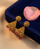 Gold earrings with colorful gemstones on a blue velvet stand with a pink flower petal.