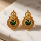 Gold earrings with green gemstones on a marble surface