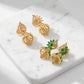 Gold earrings with green gemstones on a marble surface, branded 'Luxe'.