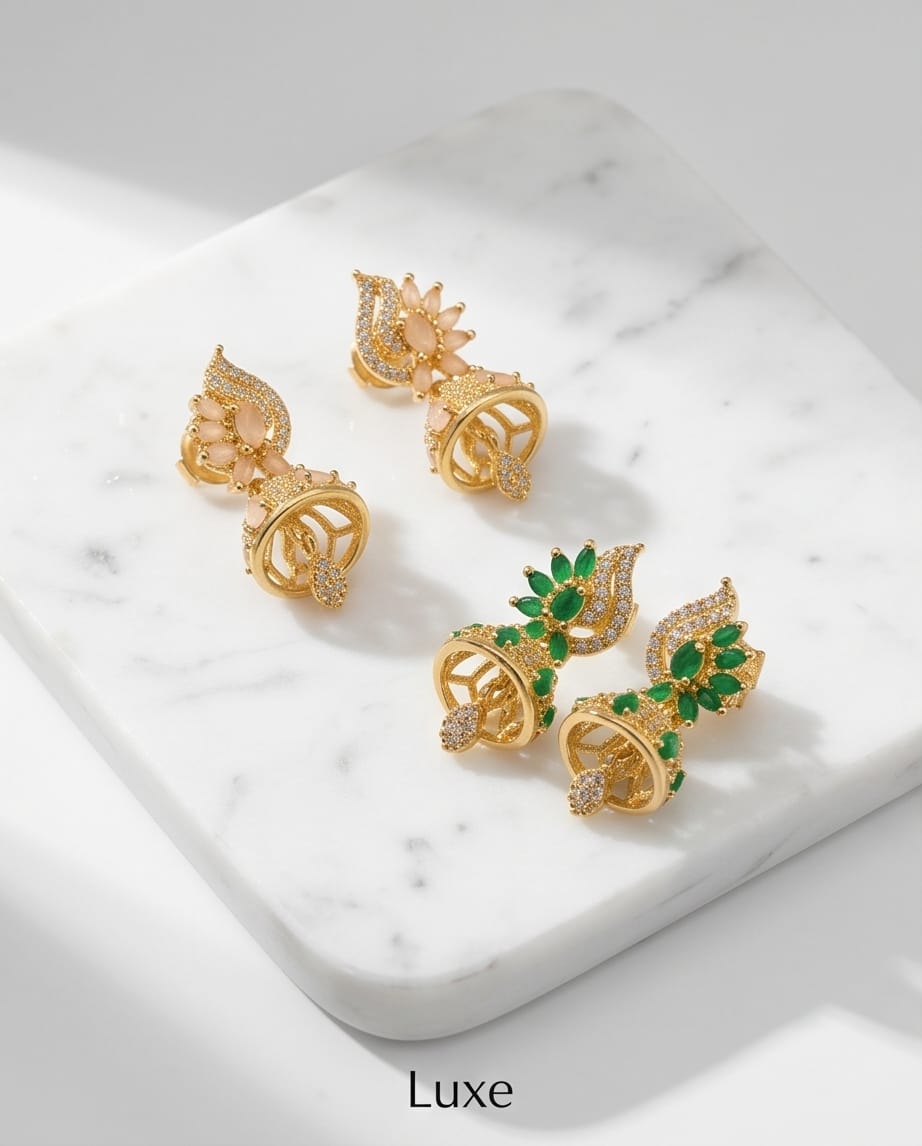 Gold earrings with green gemstones on a marble surface, branded 'Luxe'.