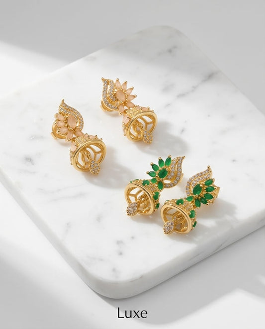 Gold earrings with green gemstones on a marble surface, branded 'Luxe'.