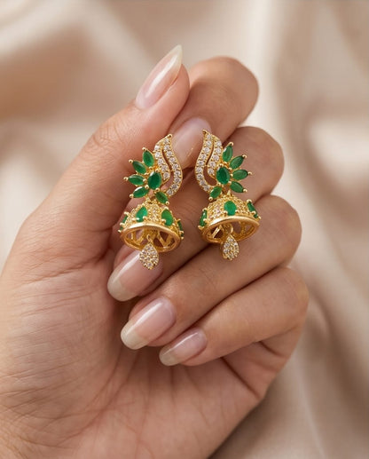 Gold earrings with green gemstones held in a hand against a beige background