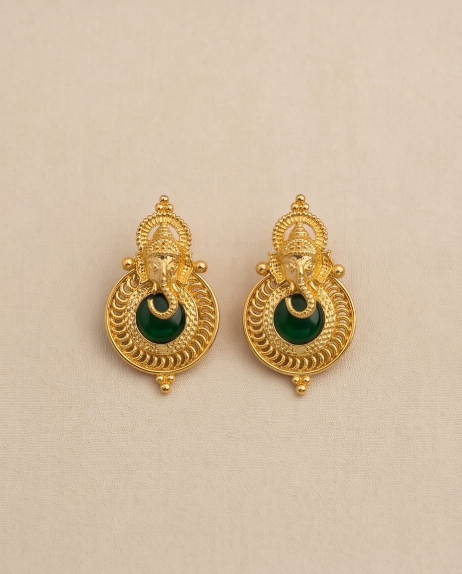 Gold earrings with green gemstones on a beige background