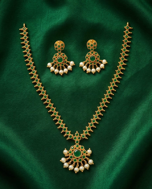Gold necklace with green gemstones and pearl-like beads on a green fabric background