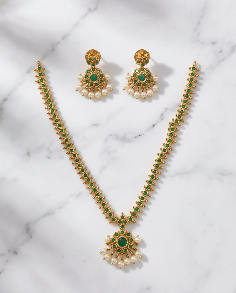 Gold necklace with green stones and pearl earrings on a marble background