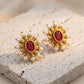 Gold earrings with red stones and pearl accents on a textured surface