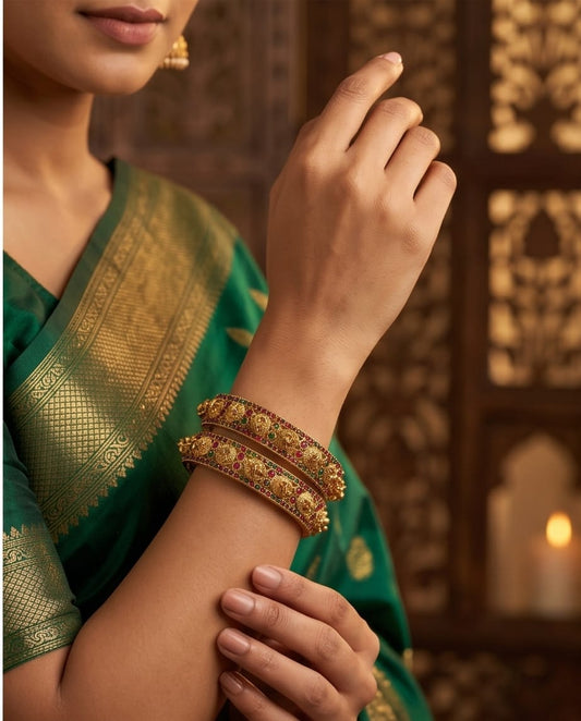 Woman wearing gold bangles on a green saree with a warm background
