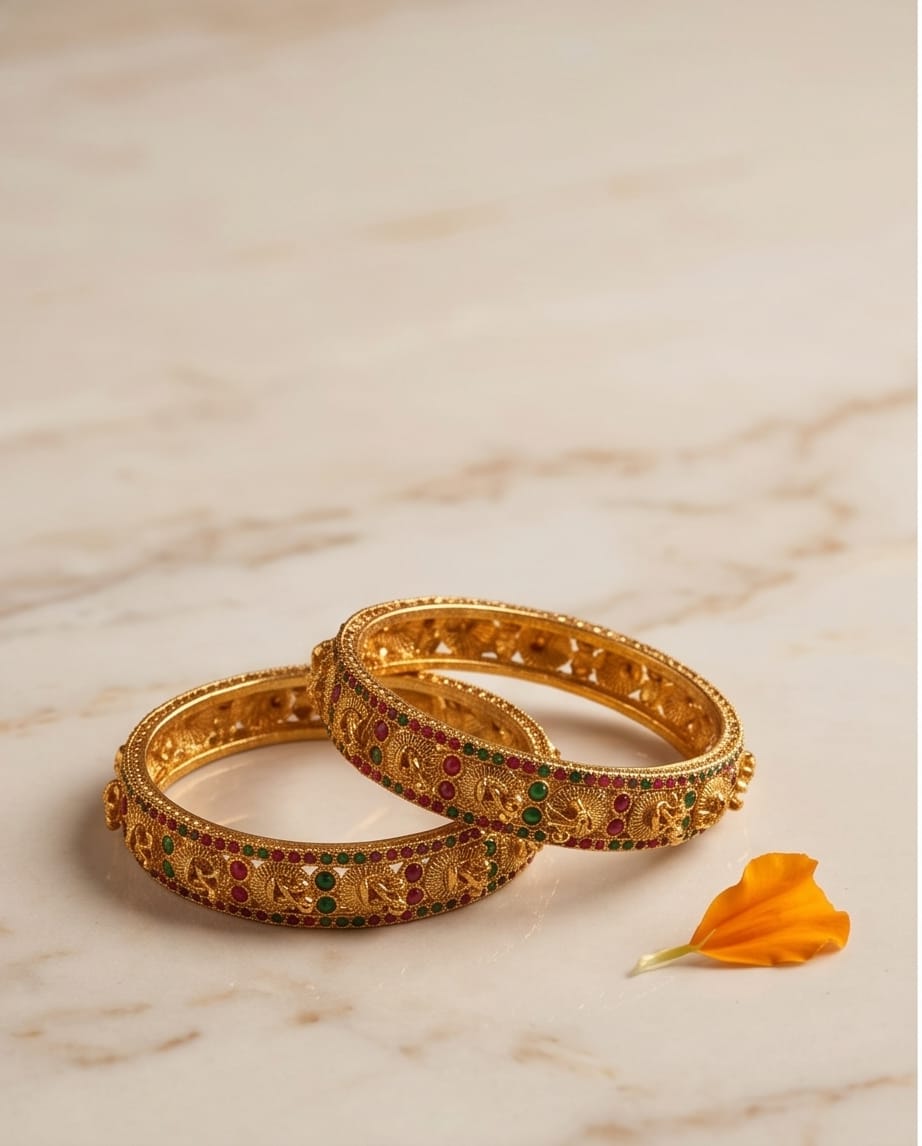 Pair of gold bangles with gemstones on a marble surface