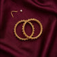 Gold hoop earrings on a maroon fabric background