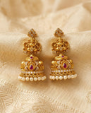 Gold earrings with pearls and red stones on a beige fabric background