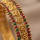 Gold bracelet with red and green gemstones on a blurred background