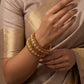 Close-up of a hand wearing gold jewelry with a beige saree background