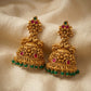 Gold earrings with red and green gemstones on a beige fabric background