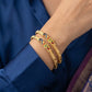Gold bracelets with colorful accents on a wrist against a blue background