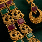 Ornate gold necklace with red and green gemstones on a dark background