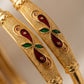 Gold bangles with red and green gemstones on a beige background